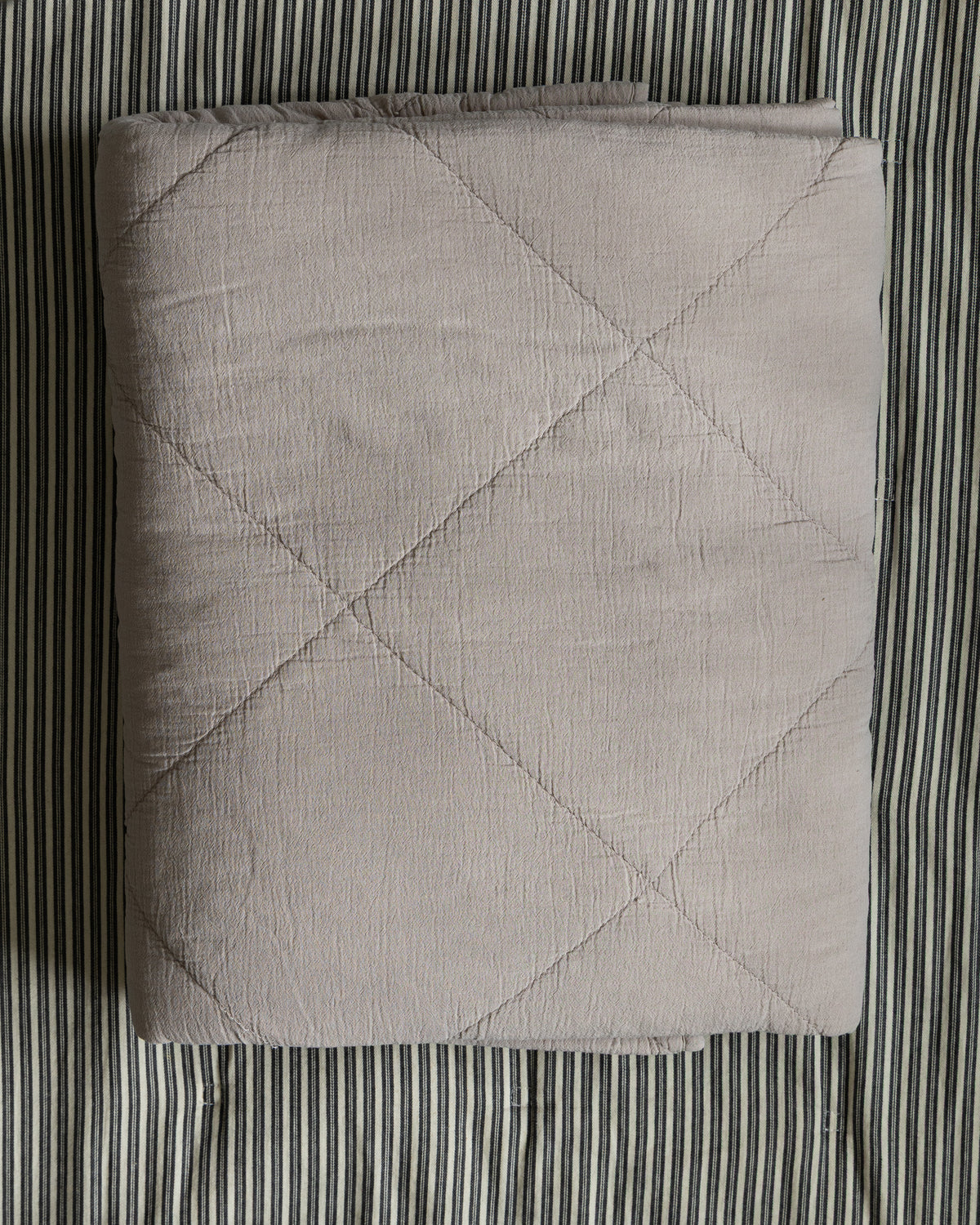 sengeteppe-beige-paa-stripet-bakgrunn