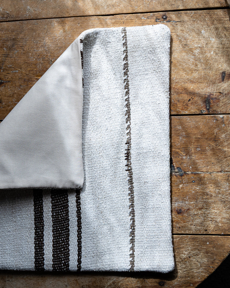 Kelim putetrekk i beige med brune striper som er brettet slik at man kan se baksiden 