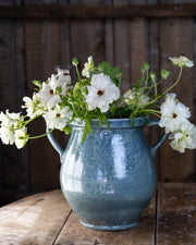 flott-blomstervase-i-blatt-med-hvite-blomster-staaende-paa-trebord