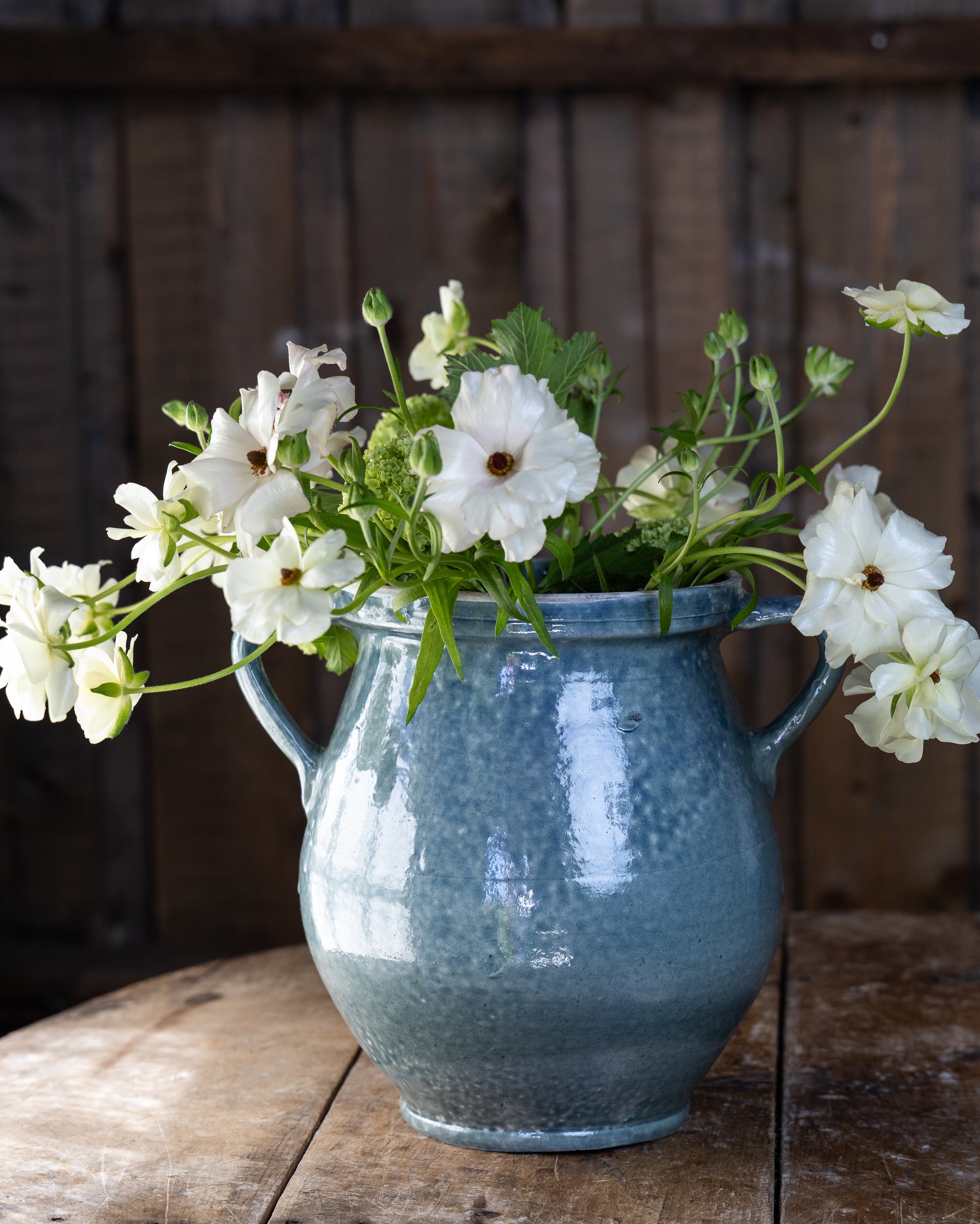 flott-blomstervase-i-blatt-med-hvite-blomster-staaende-paa-trebord