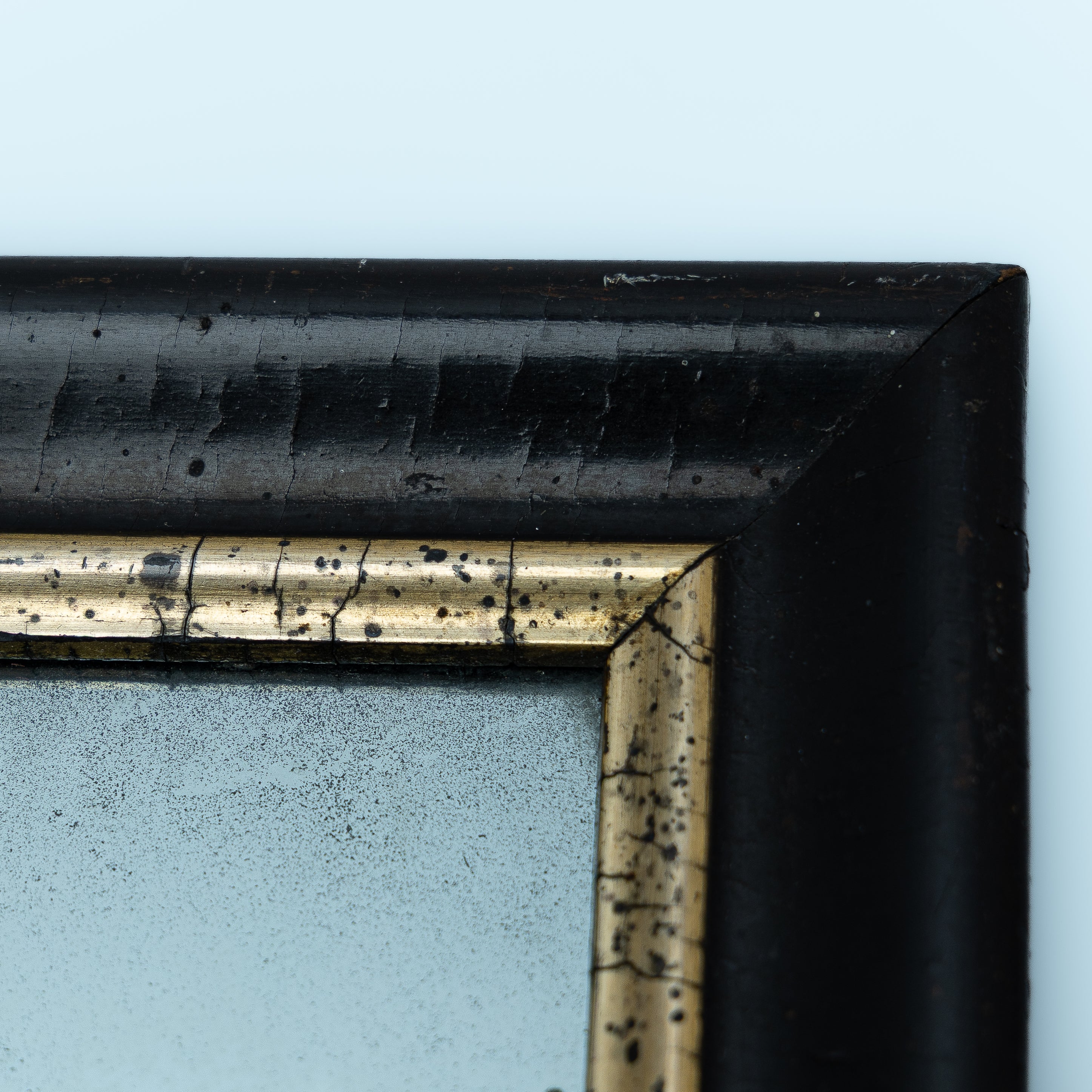 detaljbilde av rammen på et vintage speil med sort ramme og gulldetaljer