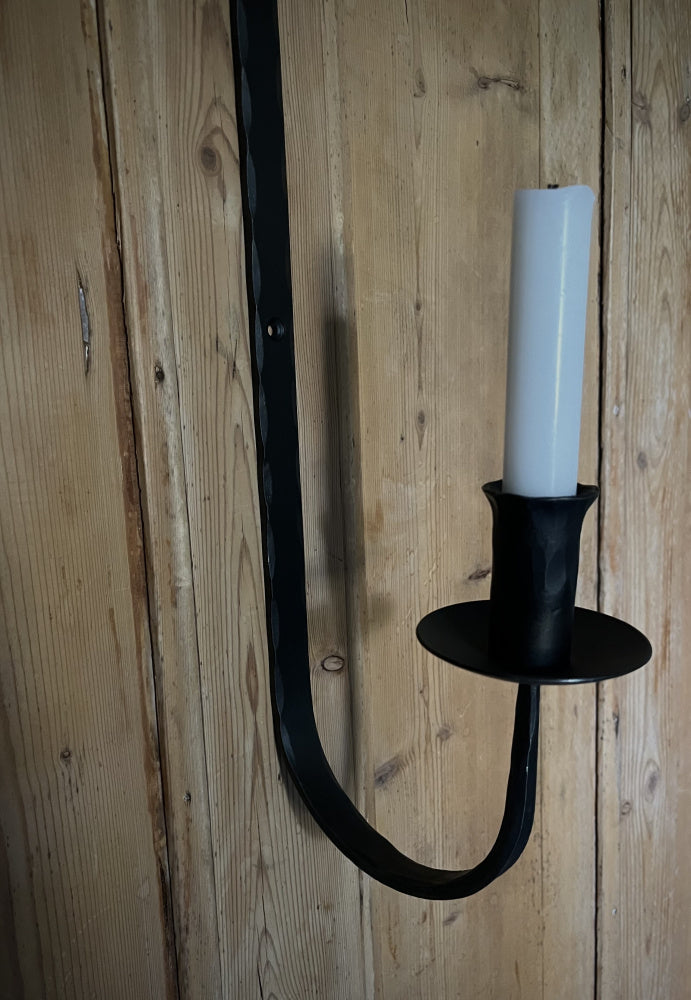 Detaljbilde av en vegghengt lysestake i smijern med et hvitt kronelys