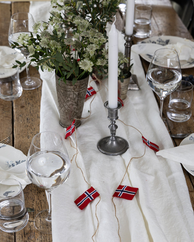 bord-dekket-med-hvit-linduk-vintage-lysestaker-lassikrus-og flaggrekke