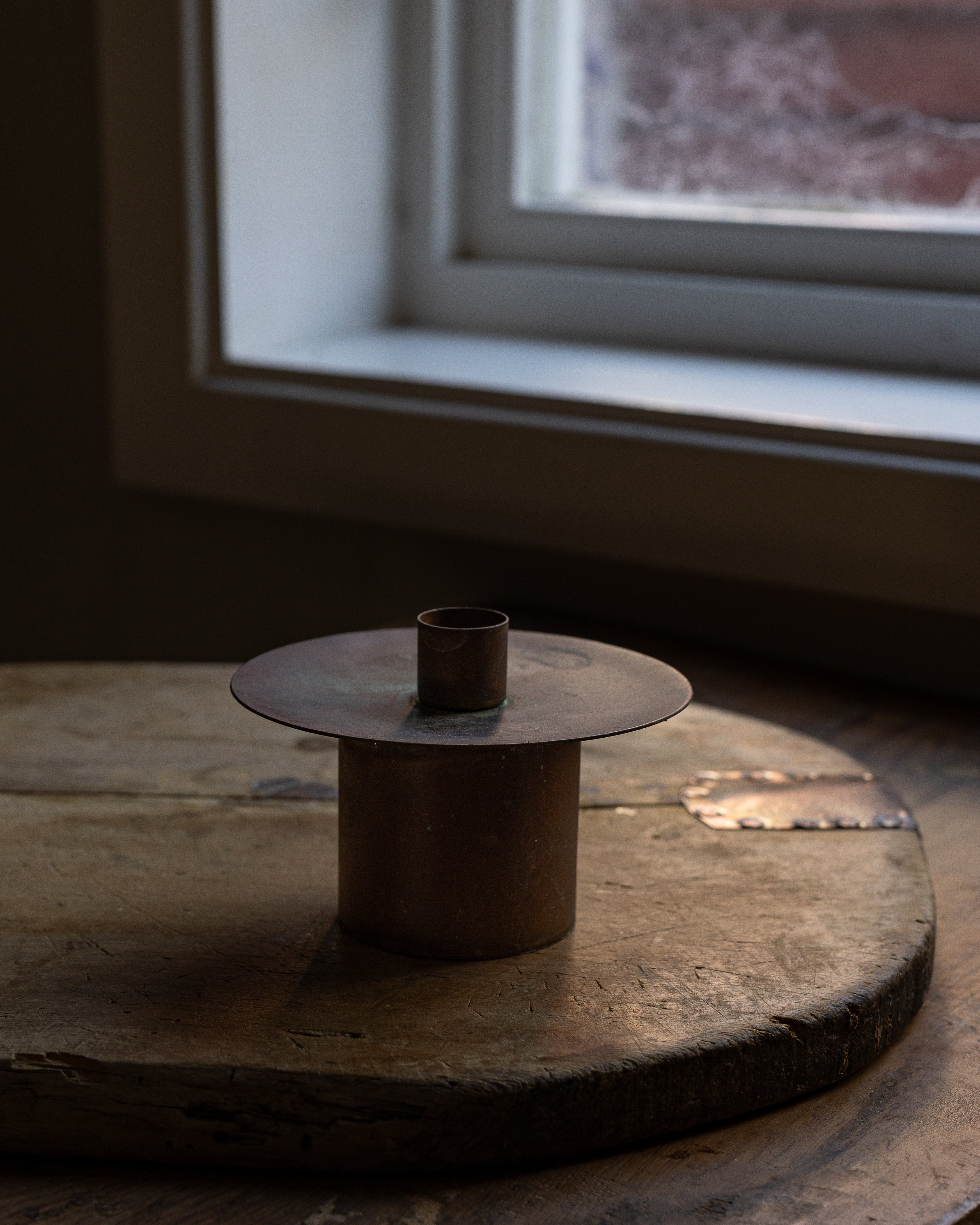 Lysestake i jern med kobberfinish stående på en fjøl nær en vinduskarm 