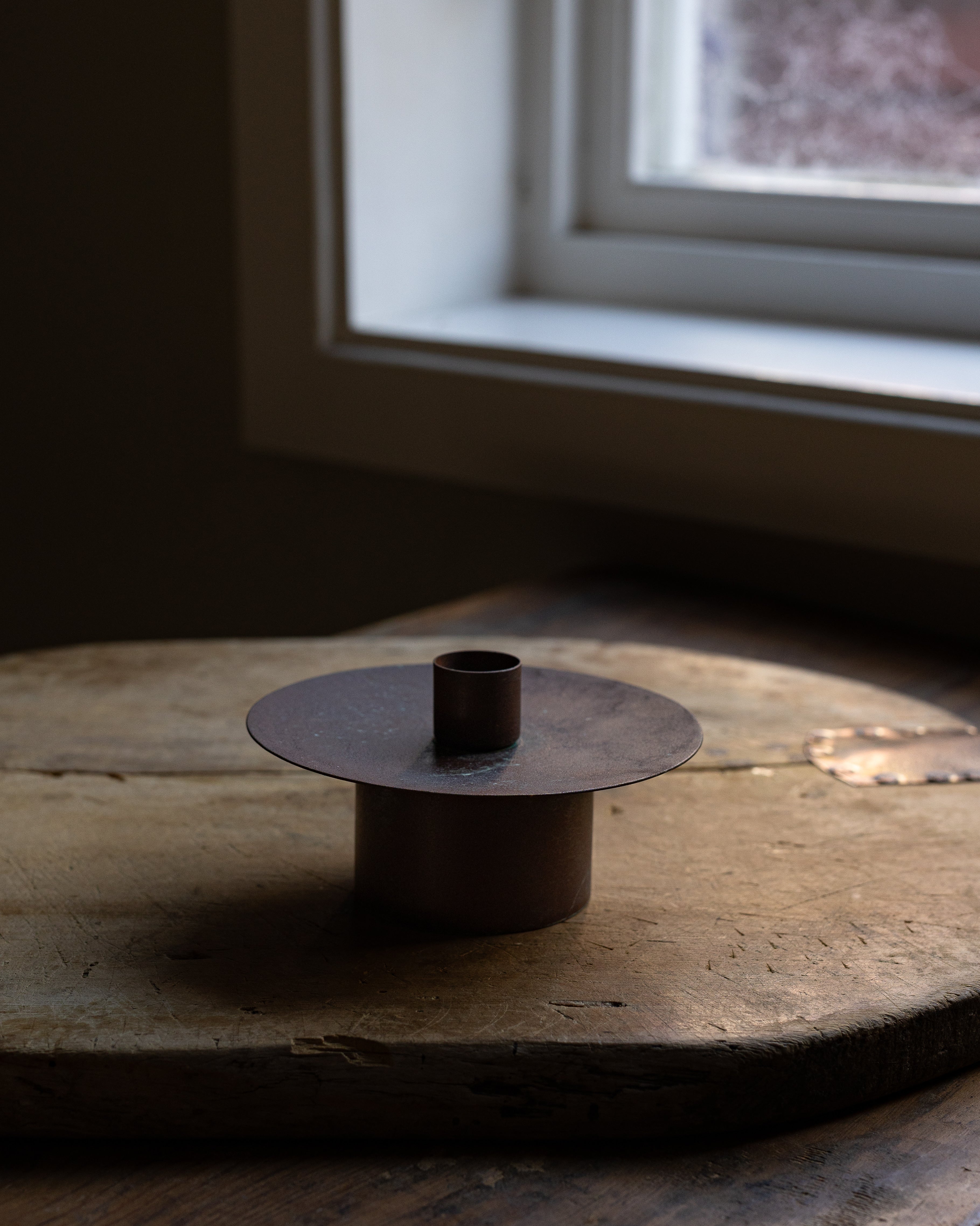 Liten rustikk lysestake i jern stående på en gammel trefjøl 