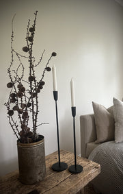 2 stk lysestaker i smijern stående på et vintage trebord ved siden av en sofa 