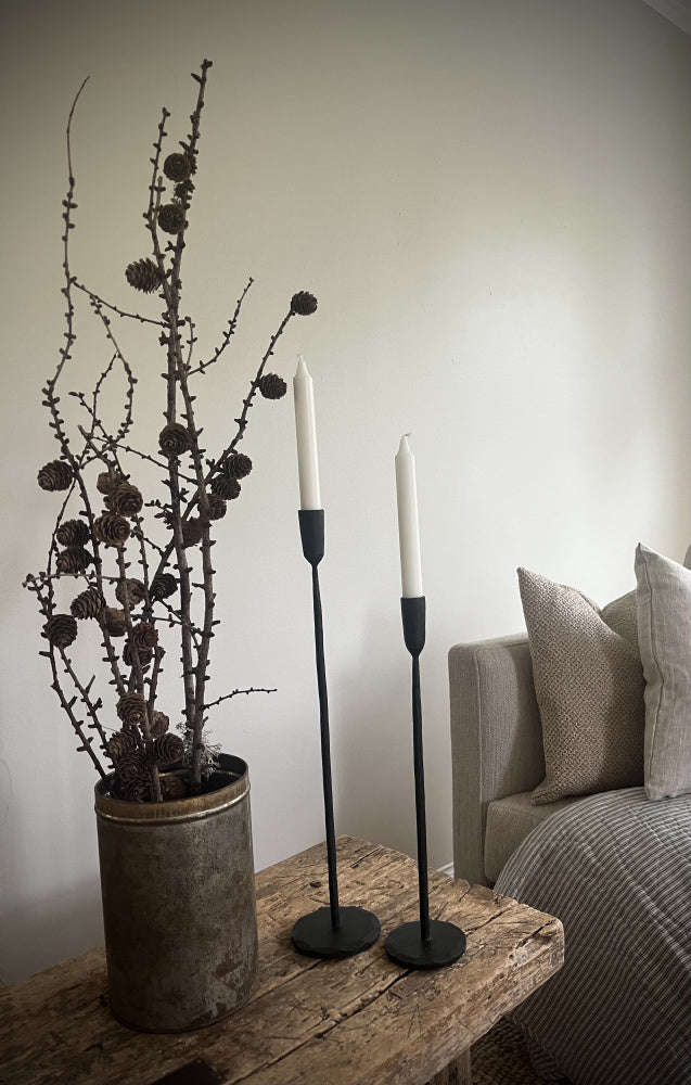 2 stk lysestaker i smijern stående på et vintage trebord ved siden av en sofa 