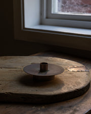 Lysestake i vakker kobberfinish stående oppå en gammel trefjøl med beslag 