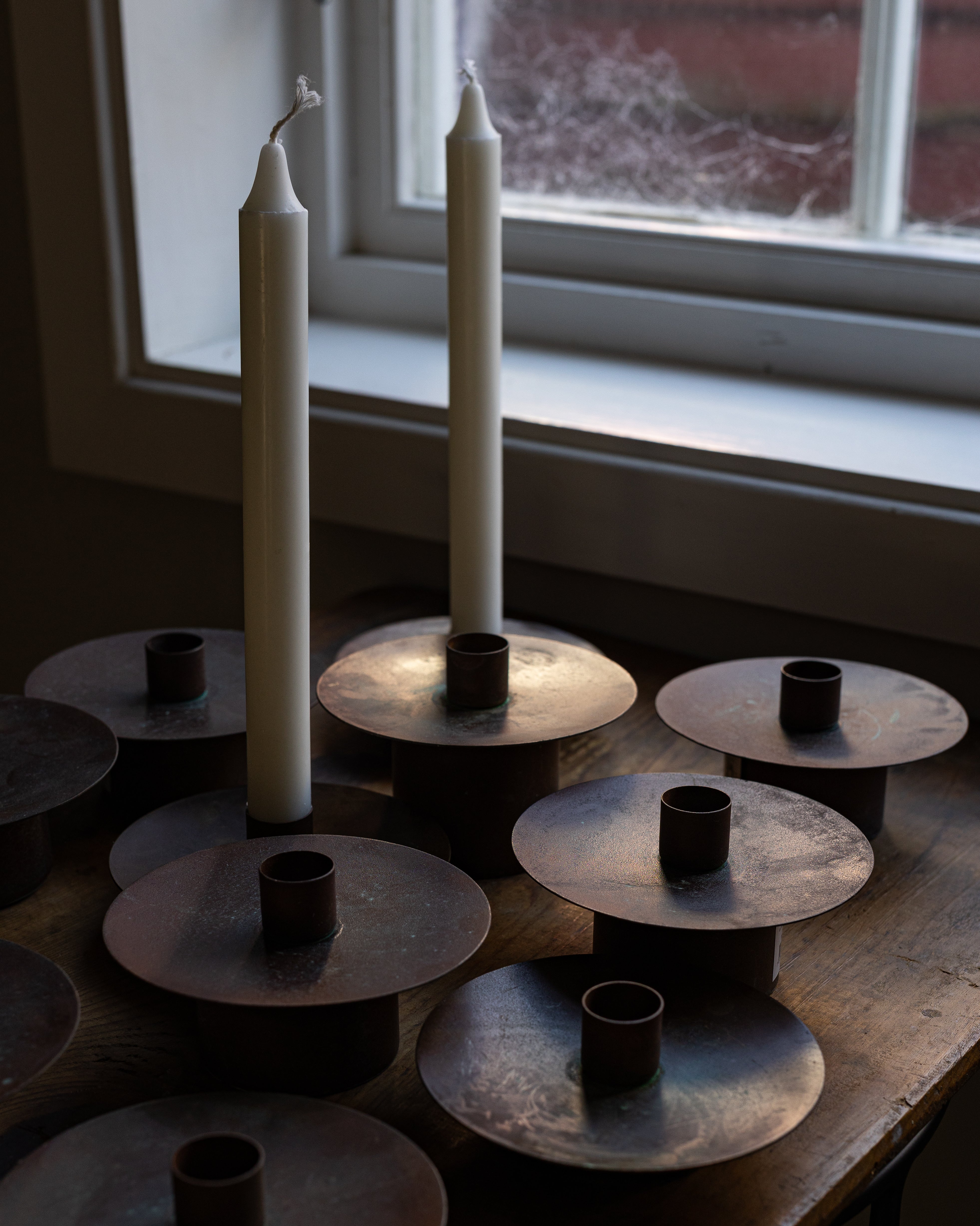 Flere rustikke lysestaker i kobberfarge samlet i en vinduskarm