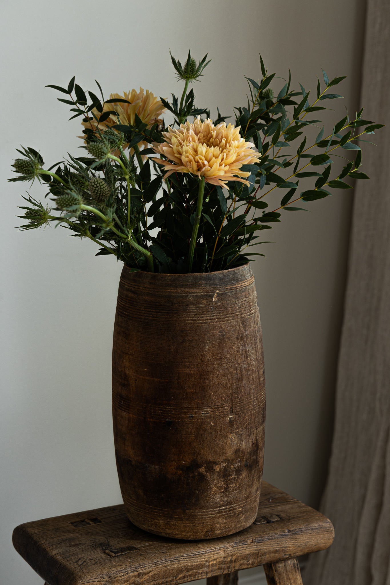 krukke-av-tre.staende-pa-krakk-med-blomster oppi