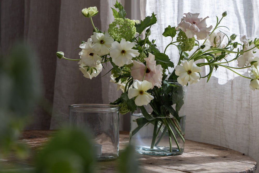 Vase i glass med sommerblomster ved siden av en mindre lyslykt i glass